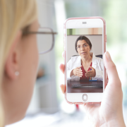 A woman looking at her phone, which shows a doctor on in a telehealth appointment